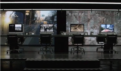 An interactive museum-style installation with a row of iMacs displaying footage from Tokyo, Paris, and Pompeii.