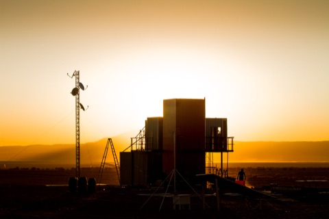 A modular production structure silhouetted against a desert sunset on location.