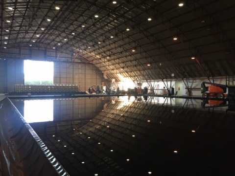 A large water tank on a soundstage, lit and ready for filming, reflecting the rigging above.